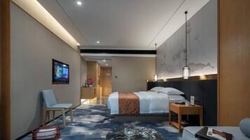 A hotel room with a bed, a seating area, a television, and a wall-mounted artwork.
