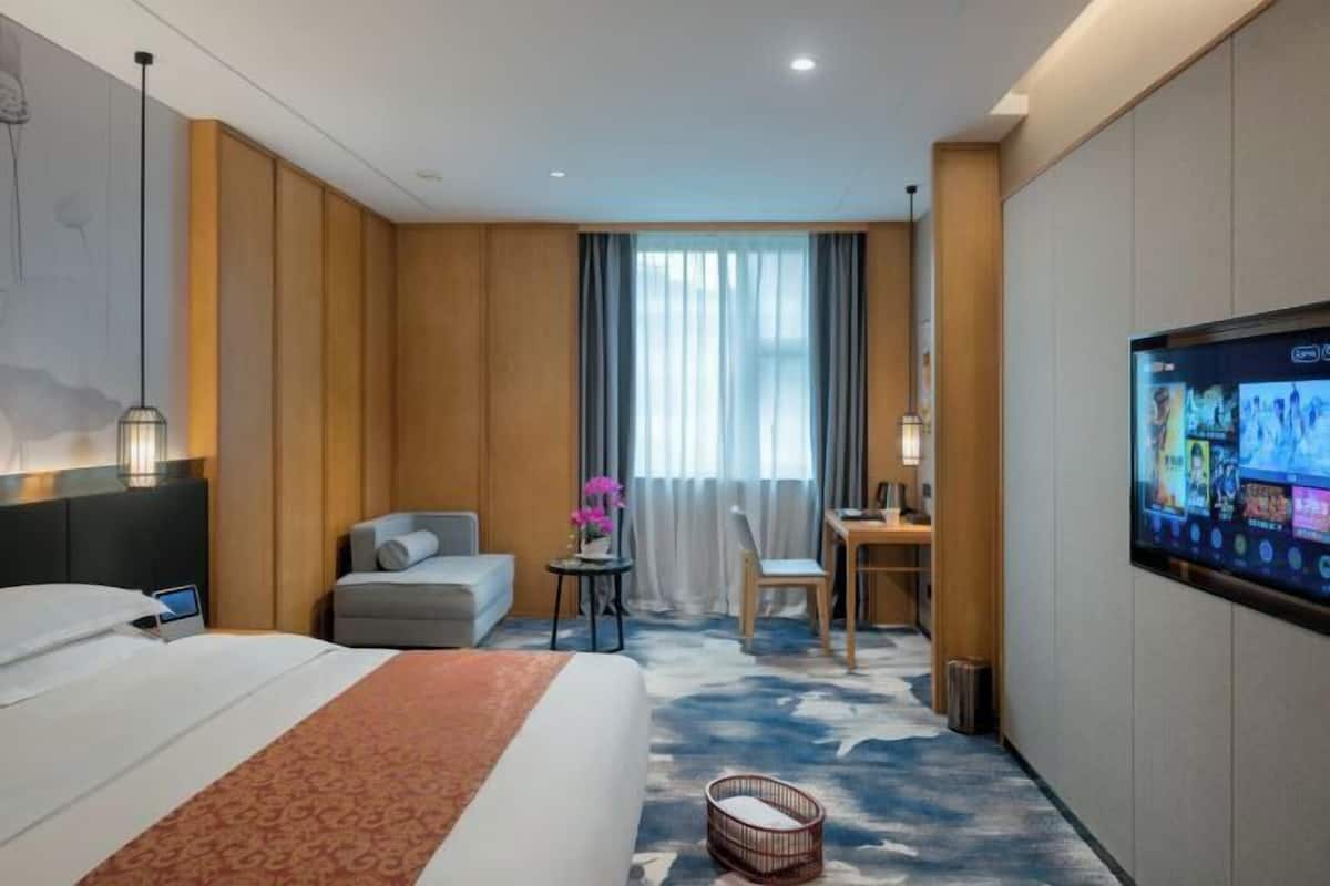 A hotel room with a bed, a desk, a chair, a TV, and a window with curtains.