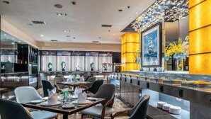 Een modern restaurant met een bar, zitplaatsen met tafels en stoelen, en een decoratieve wand met een ingelijst kunstwerk.