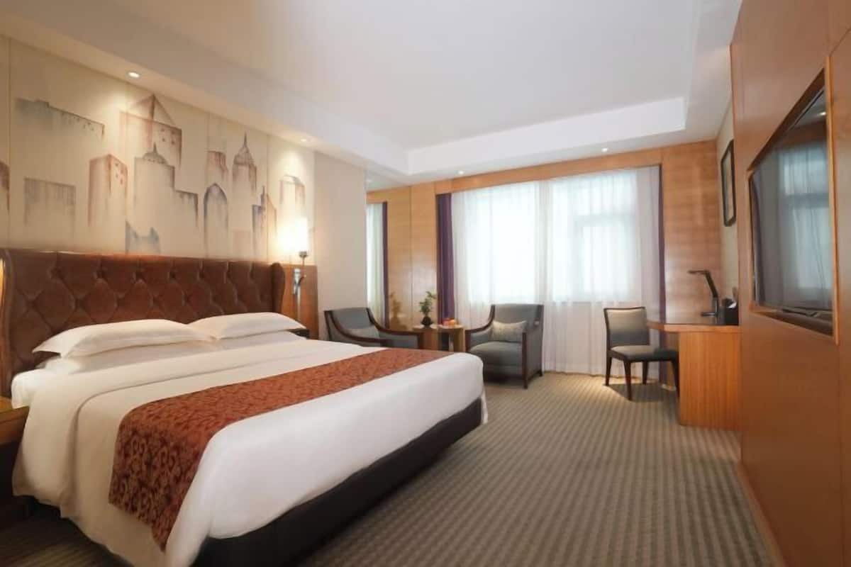 A hotel room with a large bed, a desk, two chairs, and a cityscape mural on the wall.