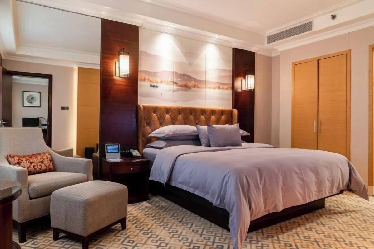 A hotel room with a large bed, a chair, a desk with a computer, and a wardrobe.