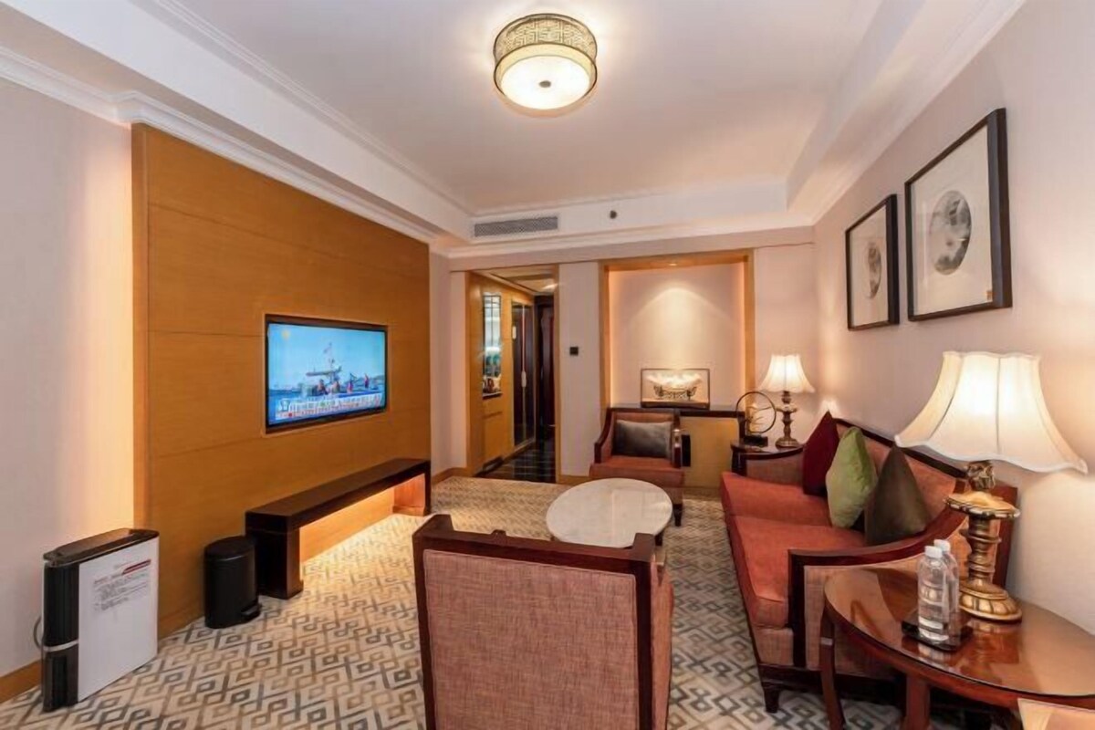 Une chambre d’hôtel équipée d’une télévision, d’un coin salon et d’un couloir menant à d’autres chambres.