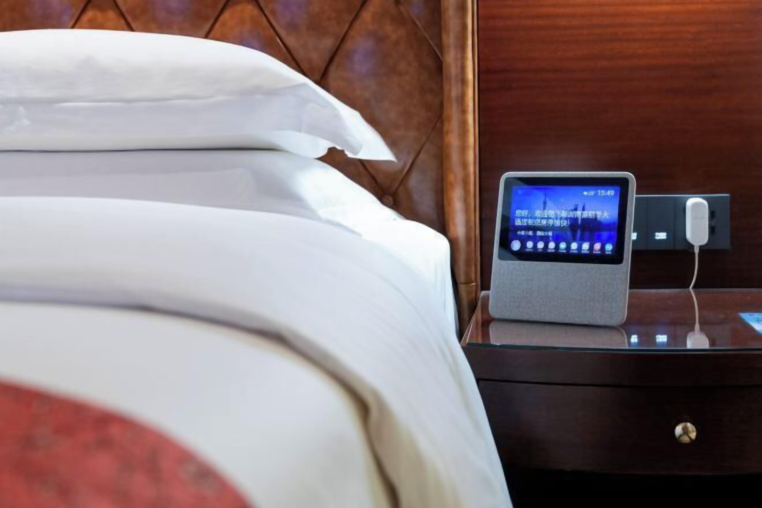 A neatly made bed with white linens, a bedside table with a digital clock, and a wooden headboard.