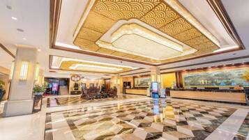 Een hotel lobby met een receptiebalie, zithoek en een gedessineerd plafond.
