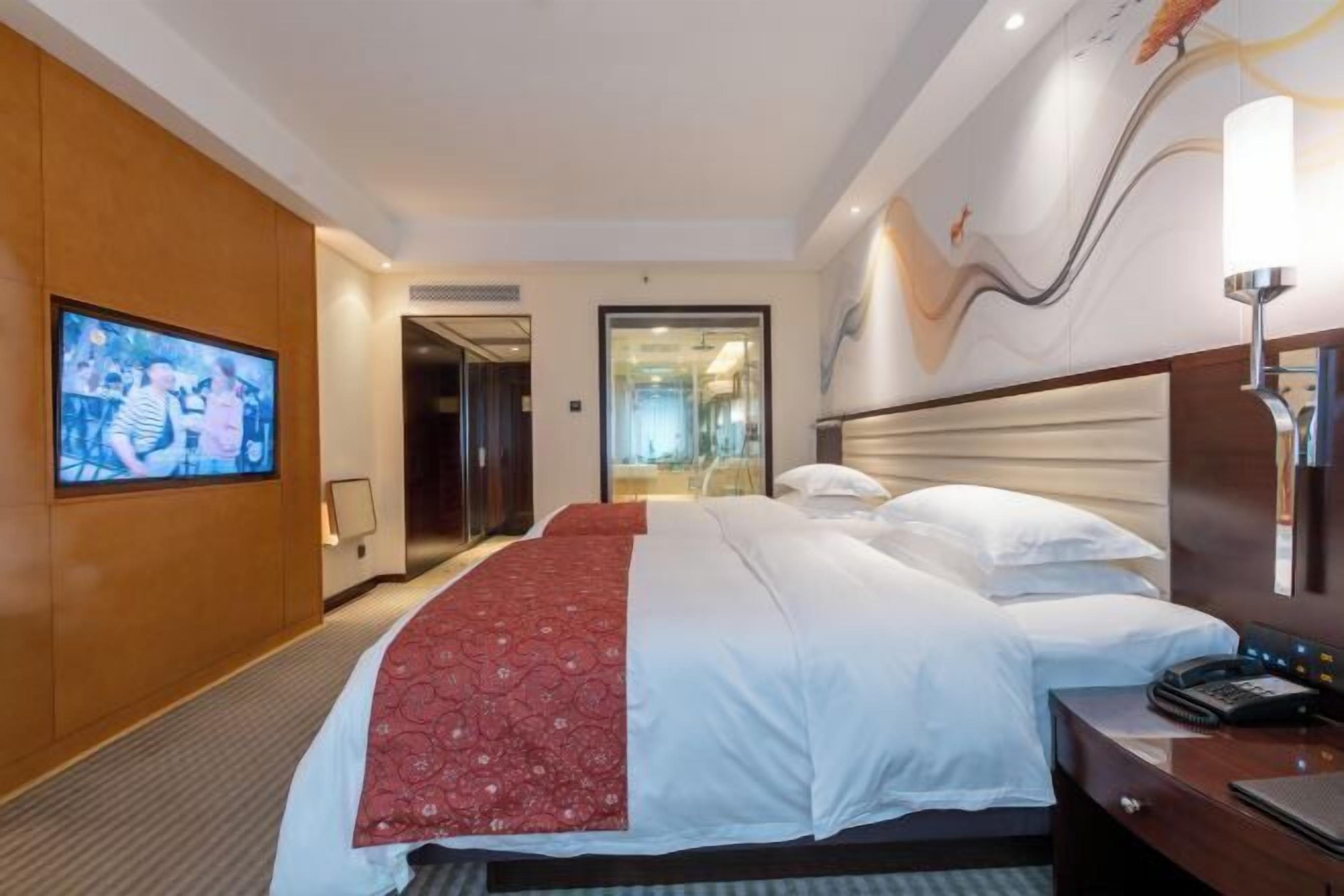 Een hotelkamer met een groot bed, een televisie aan de muur, een bureau met een telefoon en een deur naar een badkamer.