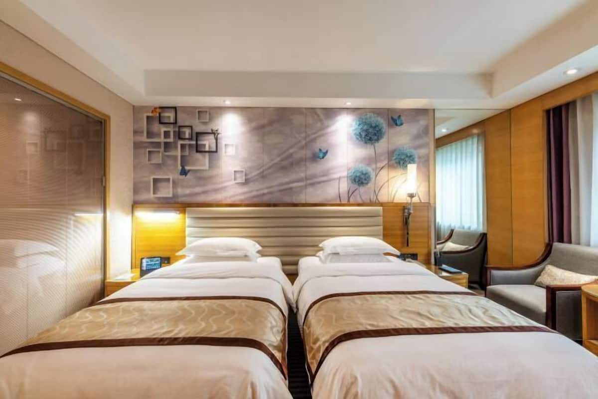 A hotel room with two beds, a headboard, a wall with decorative elements, a desk, and a chair.