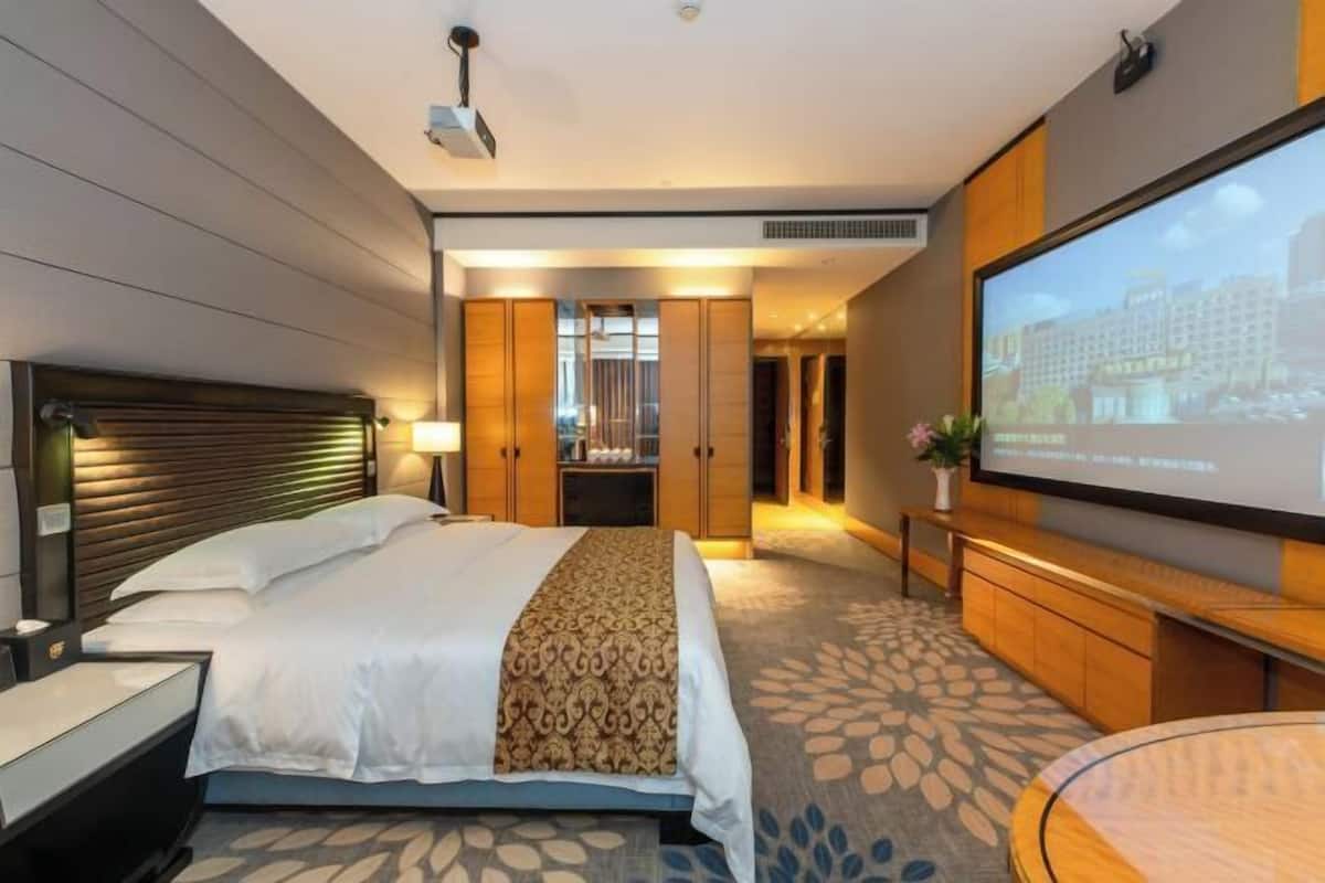 A hotel room with a bed, a TV, a desk, and a large window.