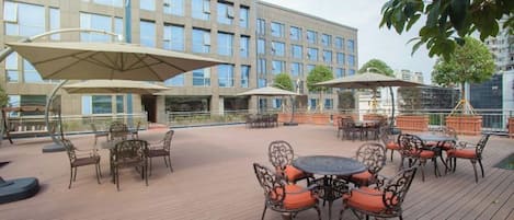 An outdoor patio with tables and chairs, umbrellas, and a building in the background.
