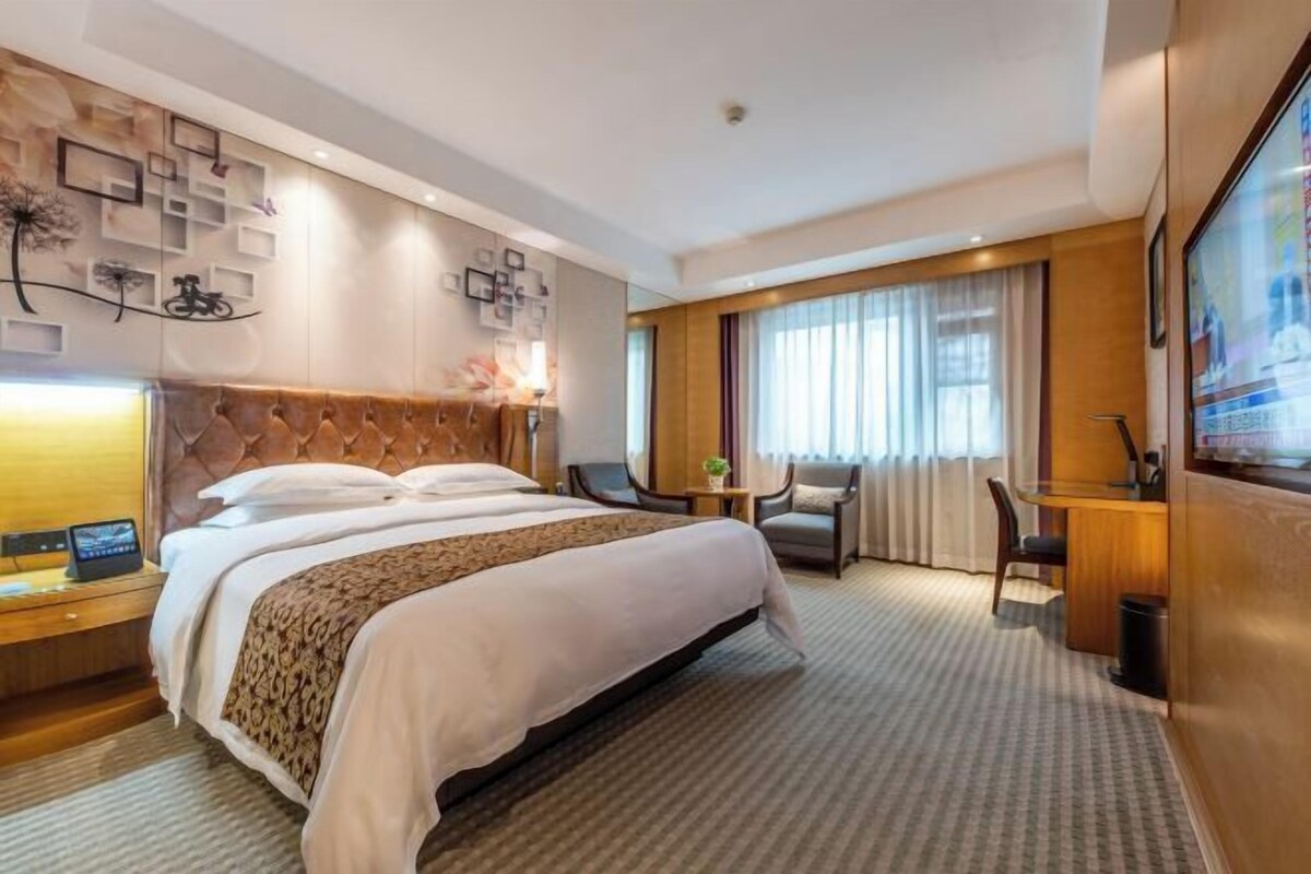 Une chambre d’hôtel avec un grand lit, un bureau avec une chaise, une télévision et un mur agrémenté d’éléments décoratifs.