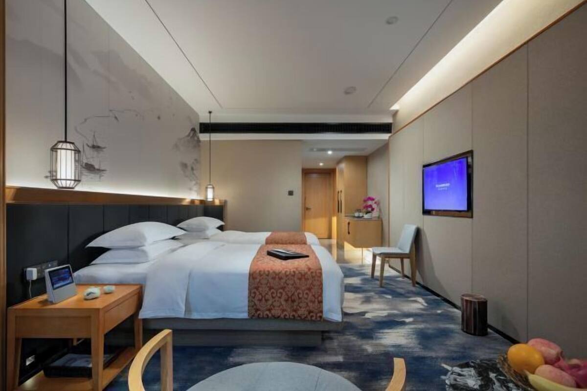A modern hotel room with a large bed, bedside tables, a desk, a chair, and a television.