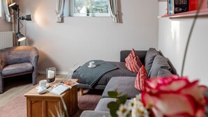 Un salon chaleureux avec un canapé, une table basse en bois sur laquelle repose un magazine, une lampe sur pied et une fenêtre avec des rideaux.