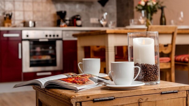 Une cuisine chaleureuse avec une table en bois, une bougie allumée, des grains de café et un magazine.