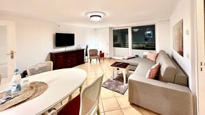 A living room with a sofa, TV, dining table, and chairs. - Penthouse-Berta - Modern vacation apartment in Westerland: Perfect for your vacation. (Sylt)