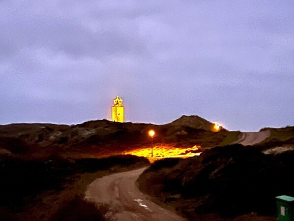 Una carretera que lleva a una colina con una estructura similar a una torre en la cima, posiblemente un faro, y un pequeño edificio a la derecha.