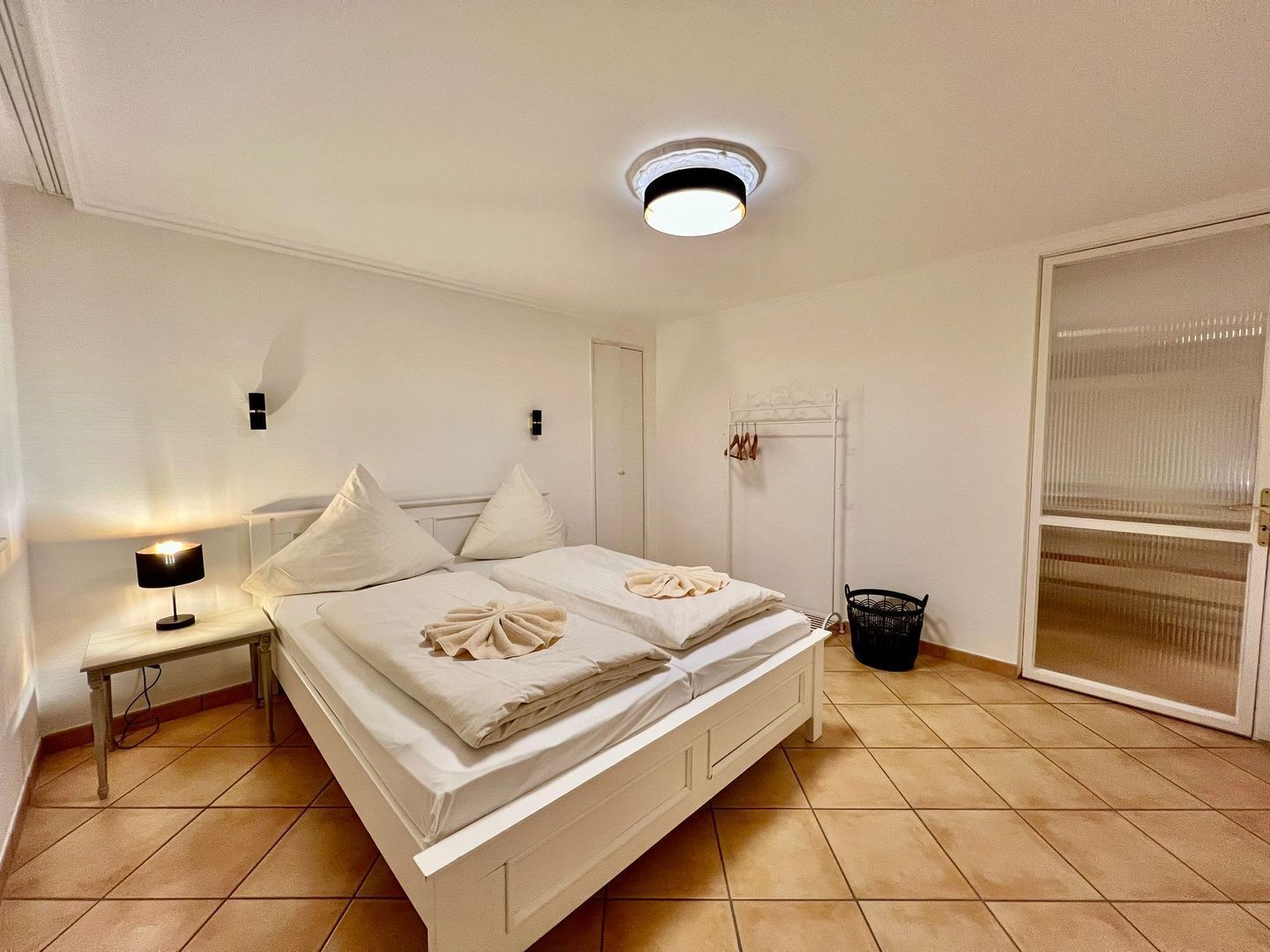 A neatly arranged bedroom with a bed, bedside table, lamp, and a window with blinds.