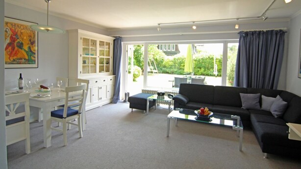 A modern living room with a dining area, large windows, and a view of the outdoors. - Brise-Sylt - The vacation apartment "Brise-Sylt" is situated at ground level and quietly in (Wenningstedt-Braderup (Sylt))