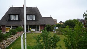 A house with a thatched roof, a stone wall, and a garden with pink flowers. - Brise-Sylt - The vacation apartment "Brise-Sylt" is situated at ground level and quietly in (Wenningstedt-Braderup (Sylt))