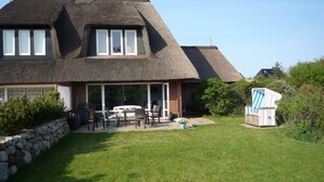 A house with a thatched roof, a patio with outdoor furniture, and a stone wall. - Brise-Sylt - The vacation apartment "Brise-Sylt" is situated at ground level and quietly in (Wenningstedt-Braderup (Sylt))