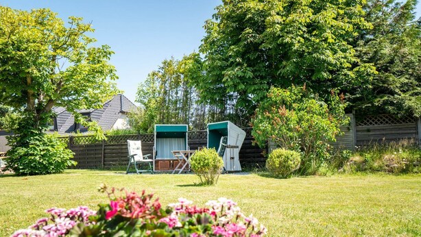 A backyard with a lawn, two outdoor seating areas, a wooden fence, and a house in the background.