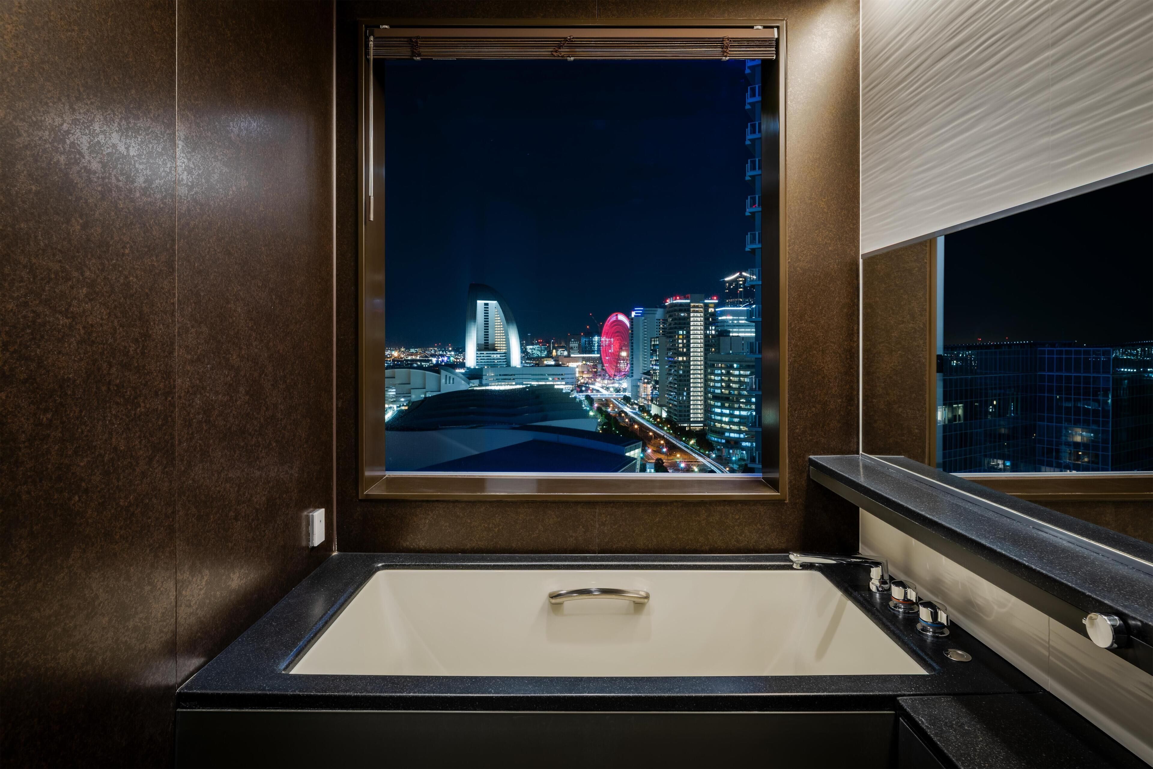 Une salle de bain moderne dotée d’une grande fenêtre offrant une vue sur la ville la nuit.