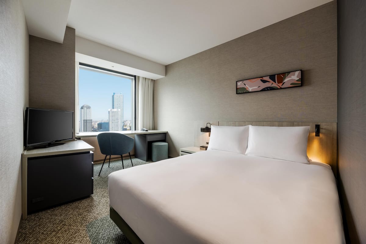 Ein Hotelzimmer mit Bett, Schreibtisch, Fernseher und Blick auf die Stadt.