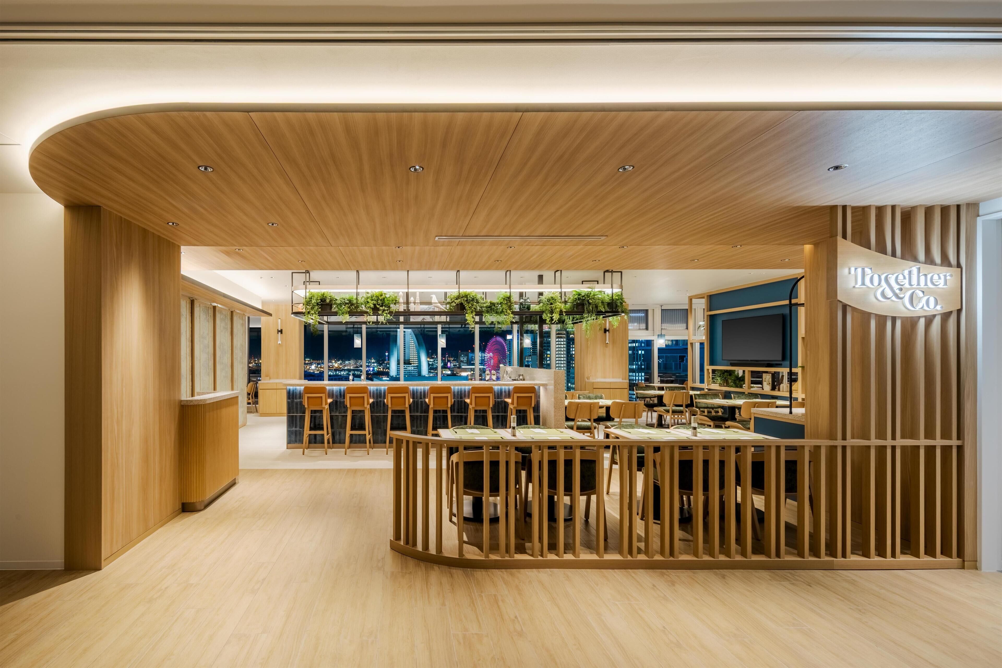 A modern restaurant with a wooden interior, a bar area, and a view of the cityscape.