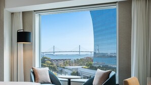 A hotel room with a large window, two chairs, a table, and a lamp. - Hilton Garden Inn Yokohama Minatomirai (Yokohama)