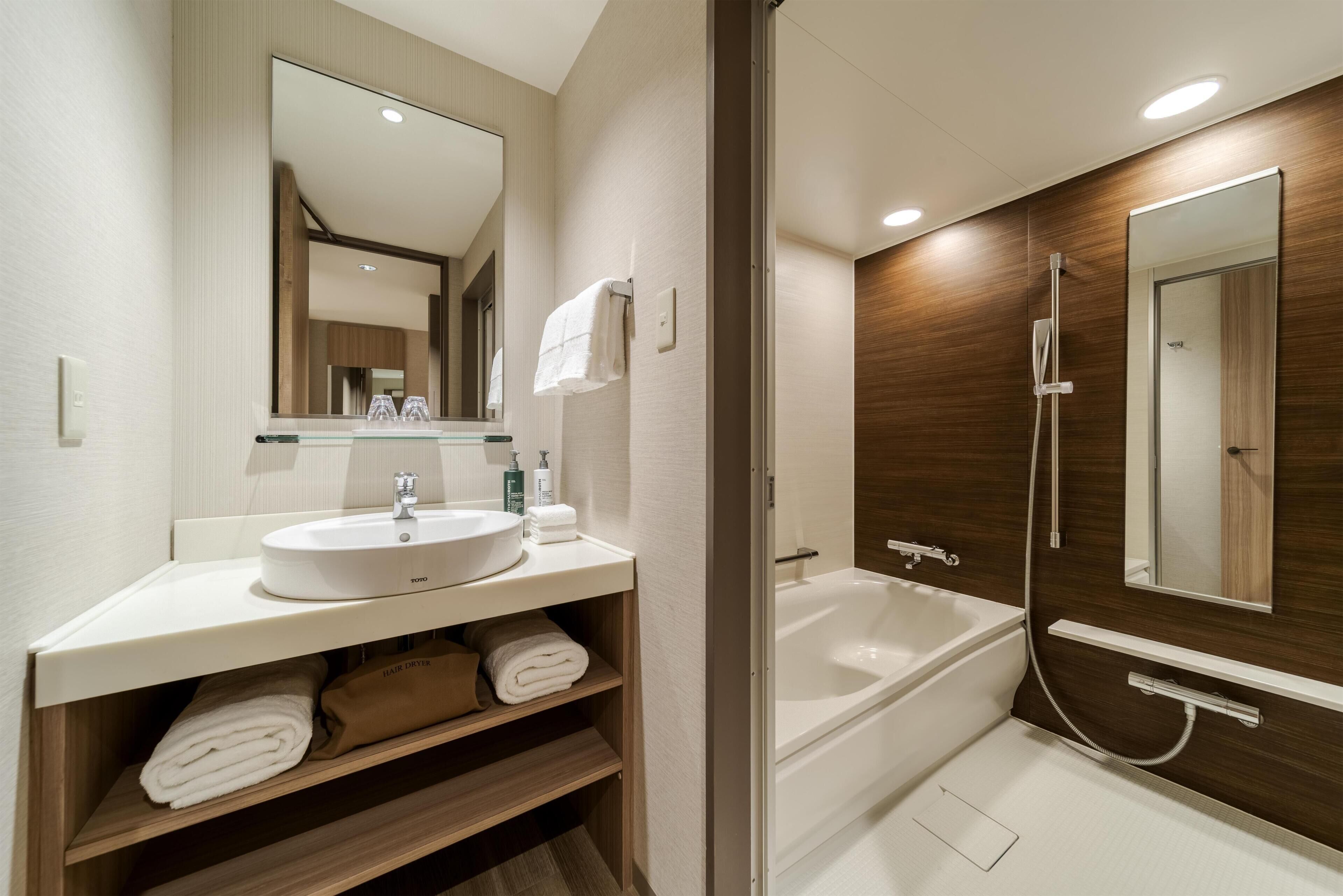 A modern bathroom with a sink, mirror, towel rack, and a bathtub with a shower head.