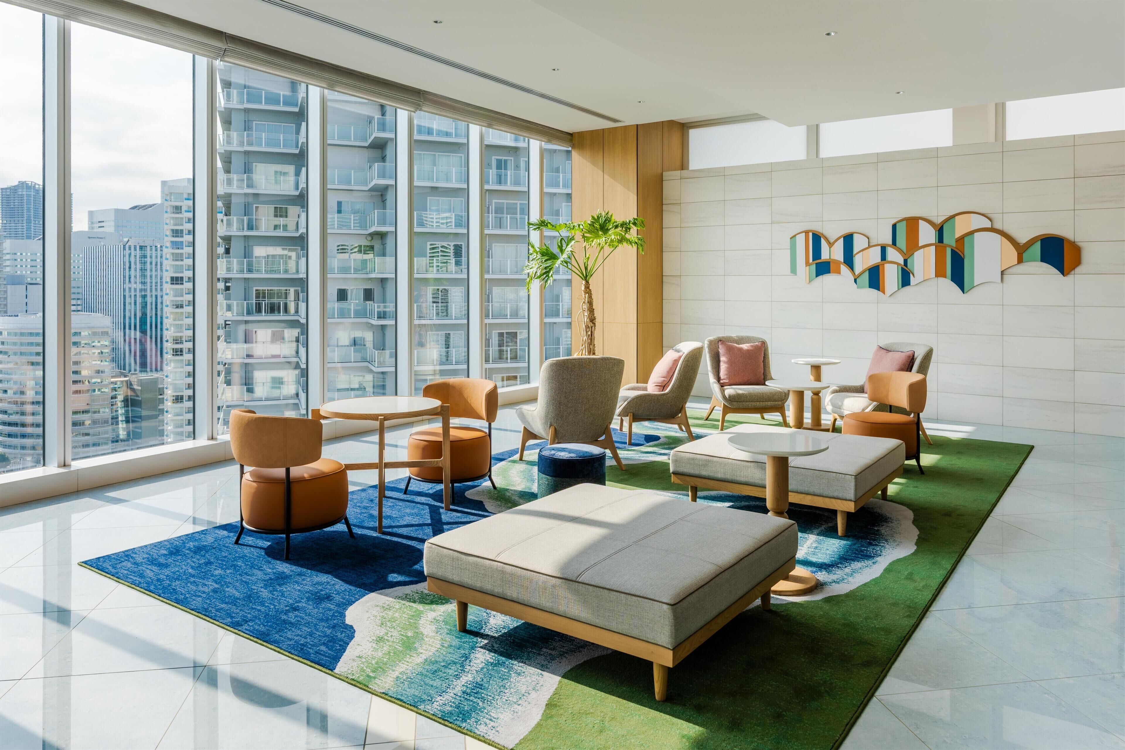 A modern hotel room with large windows, a green rug, and a city view.