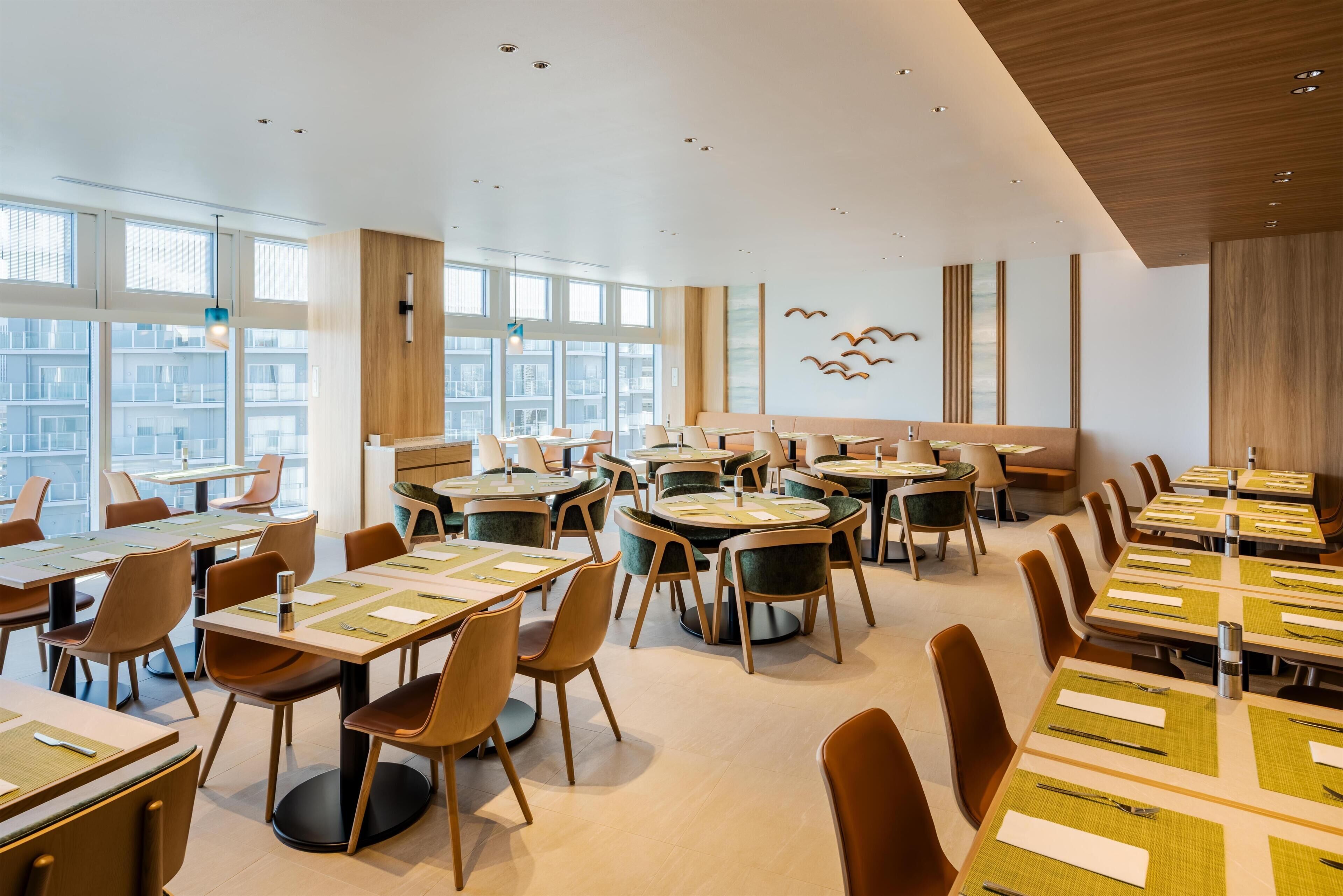 A modern dining area with multiple tables and chairs, large windows, and a city view.