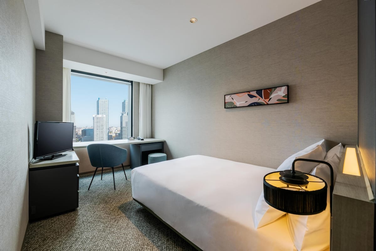 Ein Hotelzimmer mit Bett, Schreibtisch, Stuhl, Fernseher und Blick auf die Stadt.