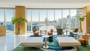 A modern hotel room with large windows, a city view, a green carpet, and a variety of seating options. - Hilton Garden Inn Yokohama Minatomirai (Yokohama)