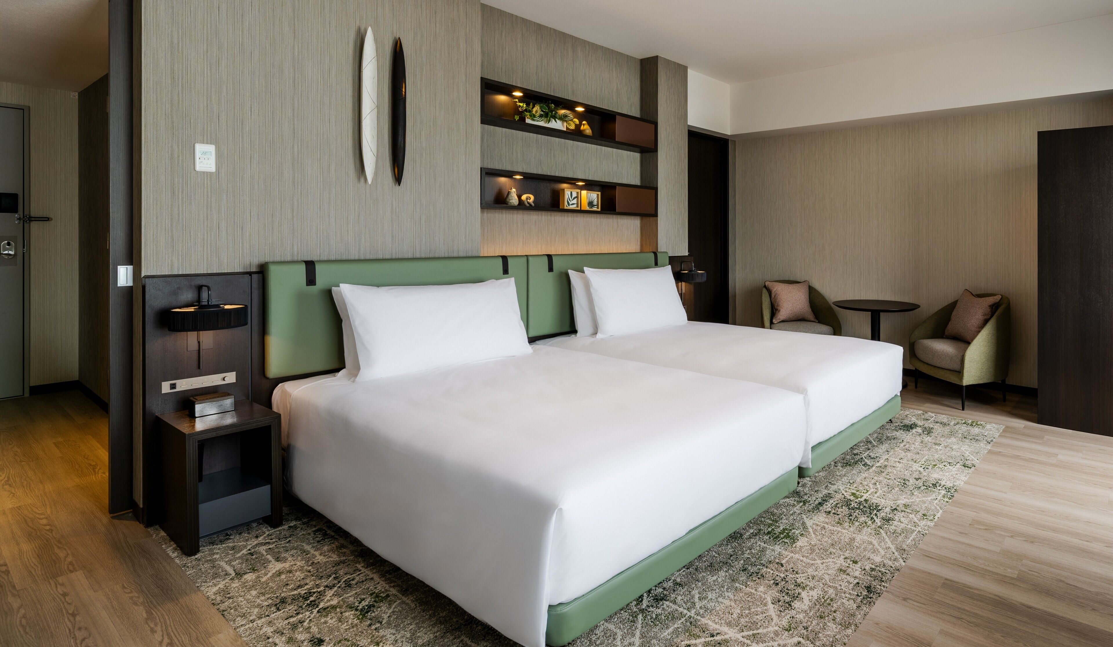 Una habitación de hotel moderna con dos camas, un escritorio, una silla y estantes empotrados con objetos decorativos.