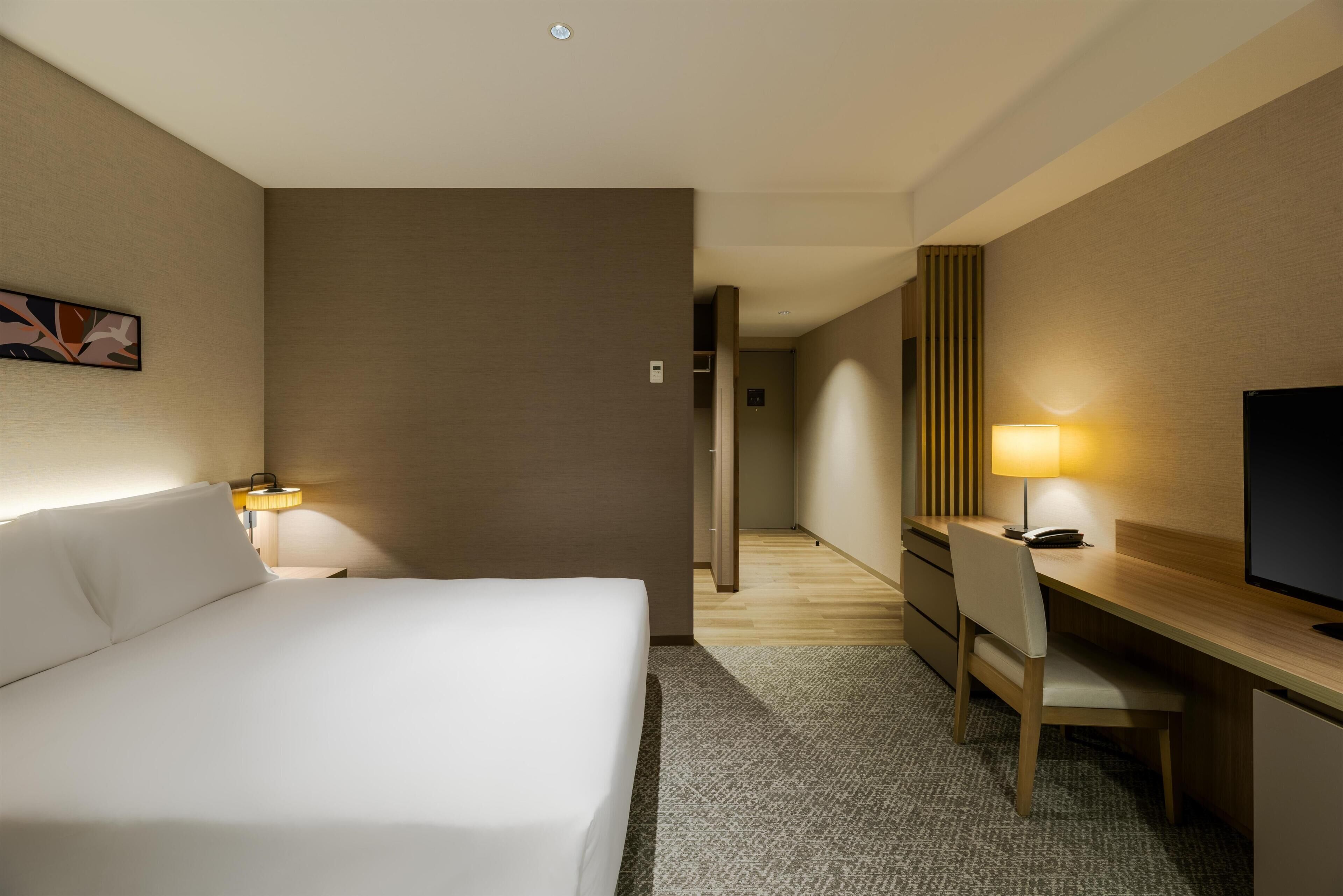 A hotel room with a bed, desk, chair, and TV.