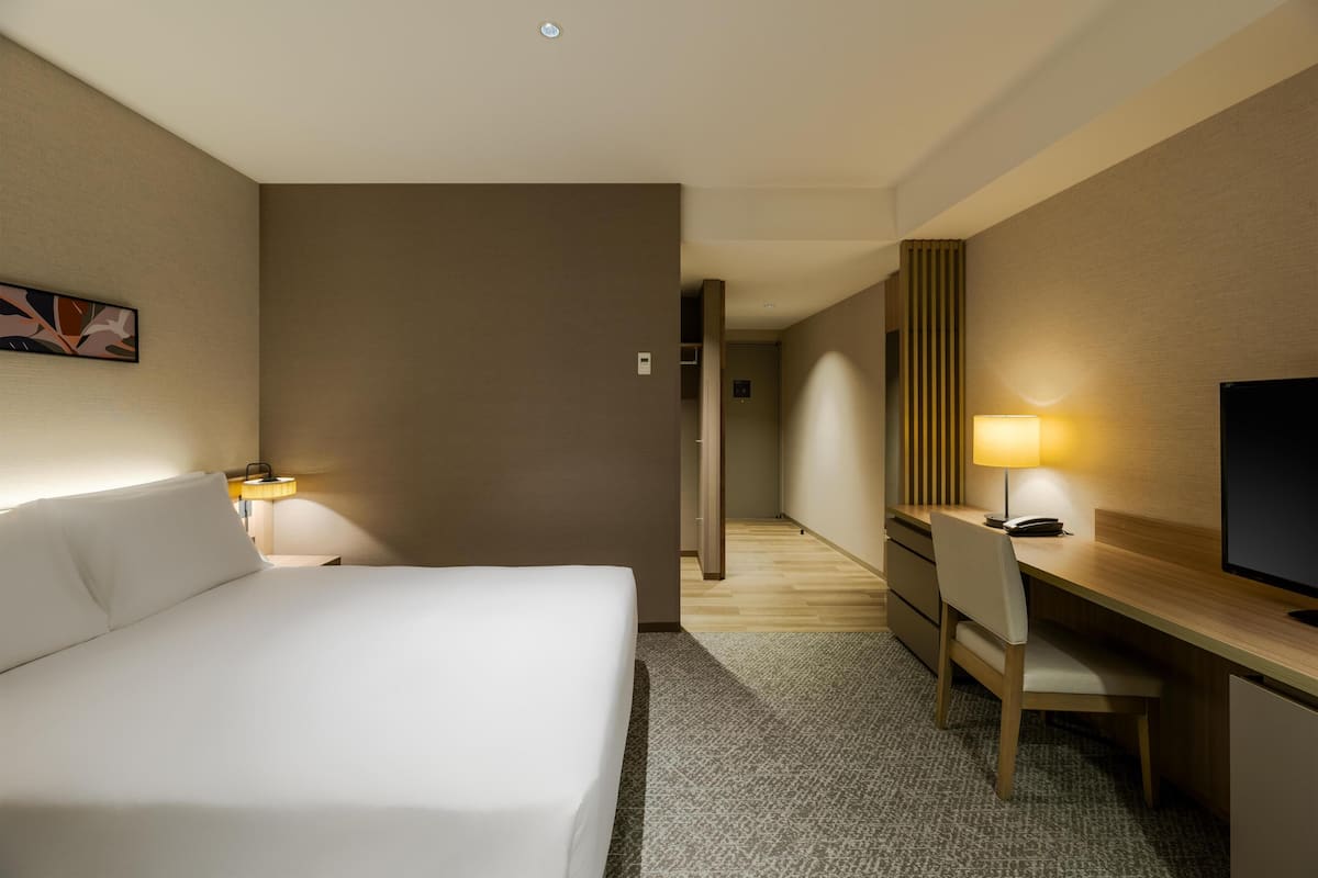Ein Hotelzimmer mit Bett, Schreibtisch, Stuhl und Fernseher.