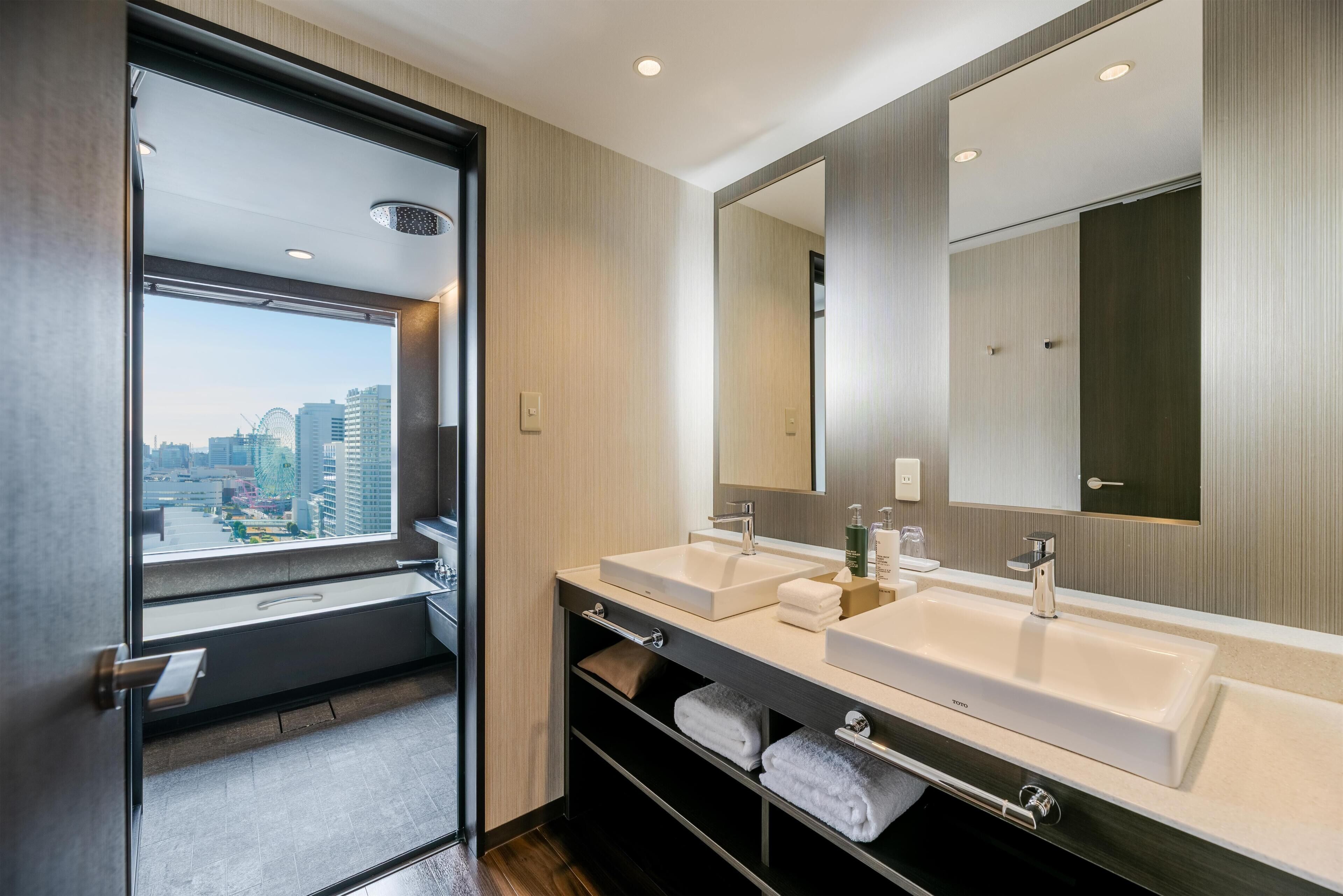 A modern bathroom with two sinks, a large mirror, and a view of the city.