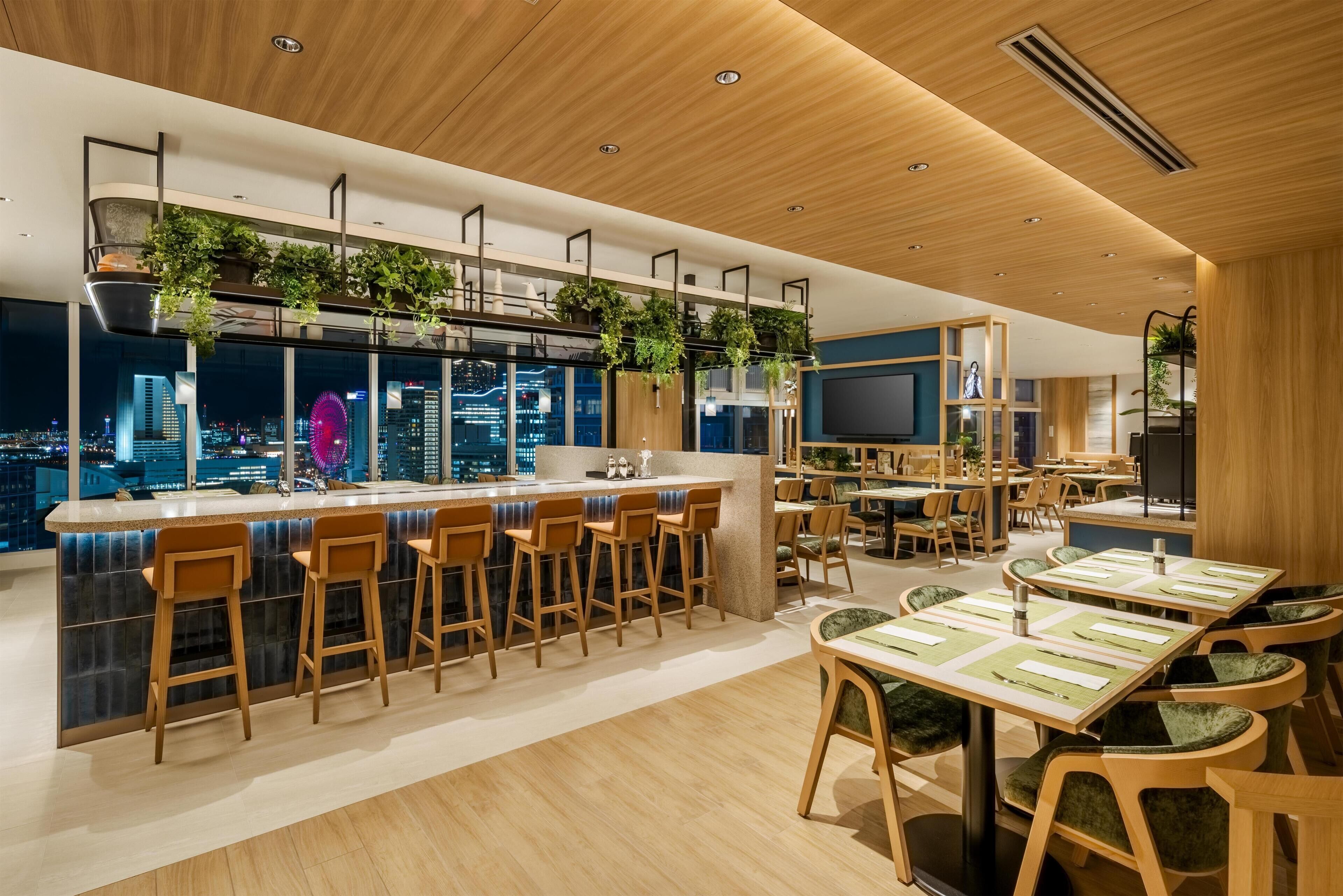 Zona de bar moderna con taburetes de madera, una barra y plantas colgantes.