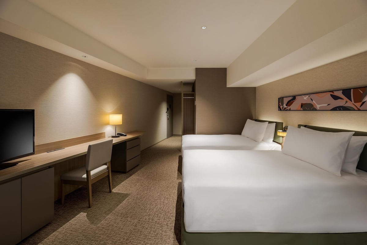 Ein Hotelzimmer mit Bett, Schreibtisch, Stuhl, Fernseher und einem Bild an der Wand.