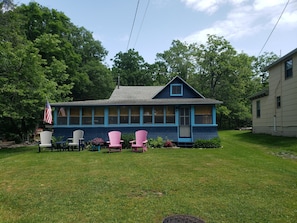 Une maison bleue avec un toit à pignon, un porche à l’avant orné de fauteuils Adirondack et un petit drapeau américain.
