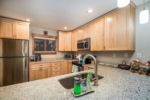 A modern kitchen with wooden cabinets, a stainless steel refrigerator, a microwave, and a granite countertop.