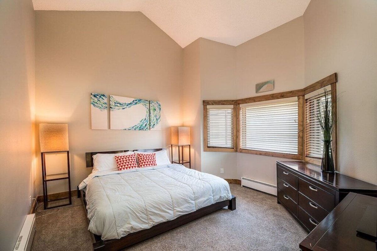 A bedroom with a bed, bedside lamps, a dresser, and a window with blinds.