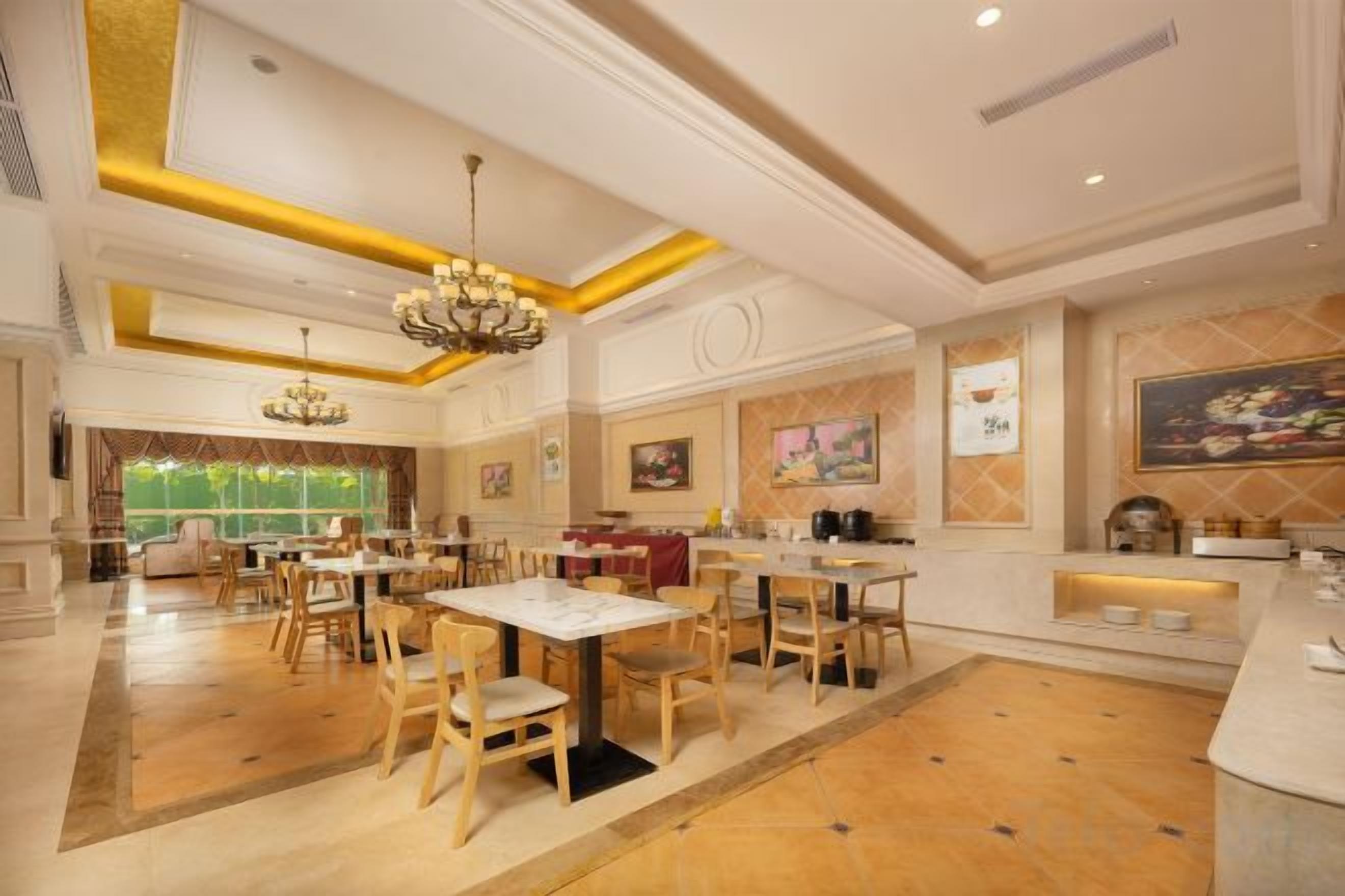 A spacious dining area with multiple tables and chairs, a chandelier, and a view of the outdoors.