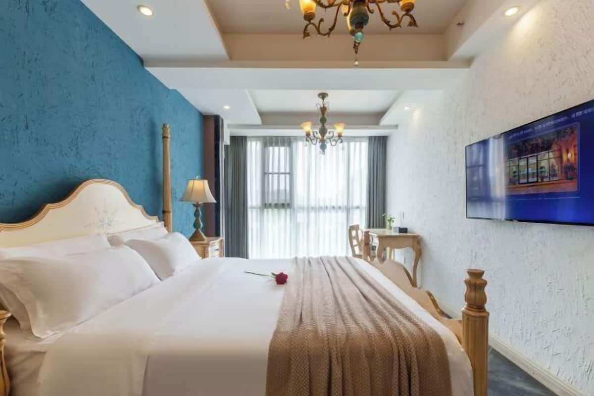 Quarto de hotel com uma cama grande, um candelabro, uma televisão e vista para o exterior pela janela.