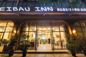 The exterior of the Eibau Inn with a large illuminated sign, large windows, and potted plants in front. - Aibao Hotel (Chongqing)
