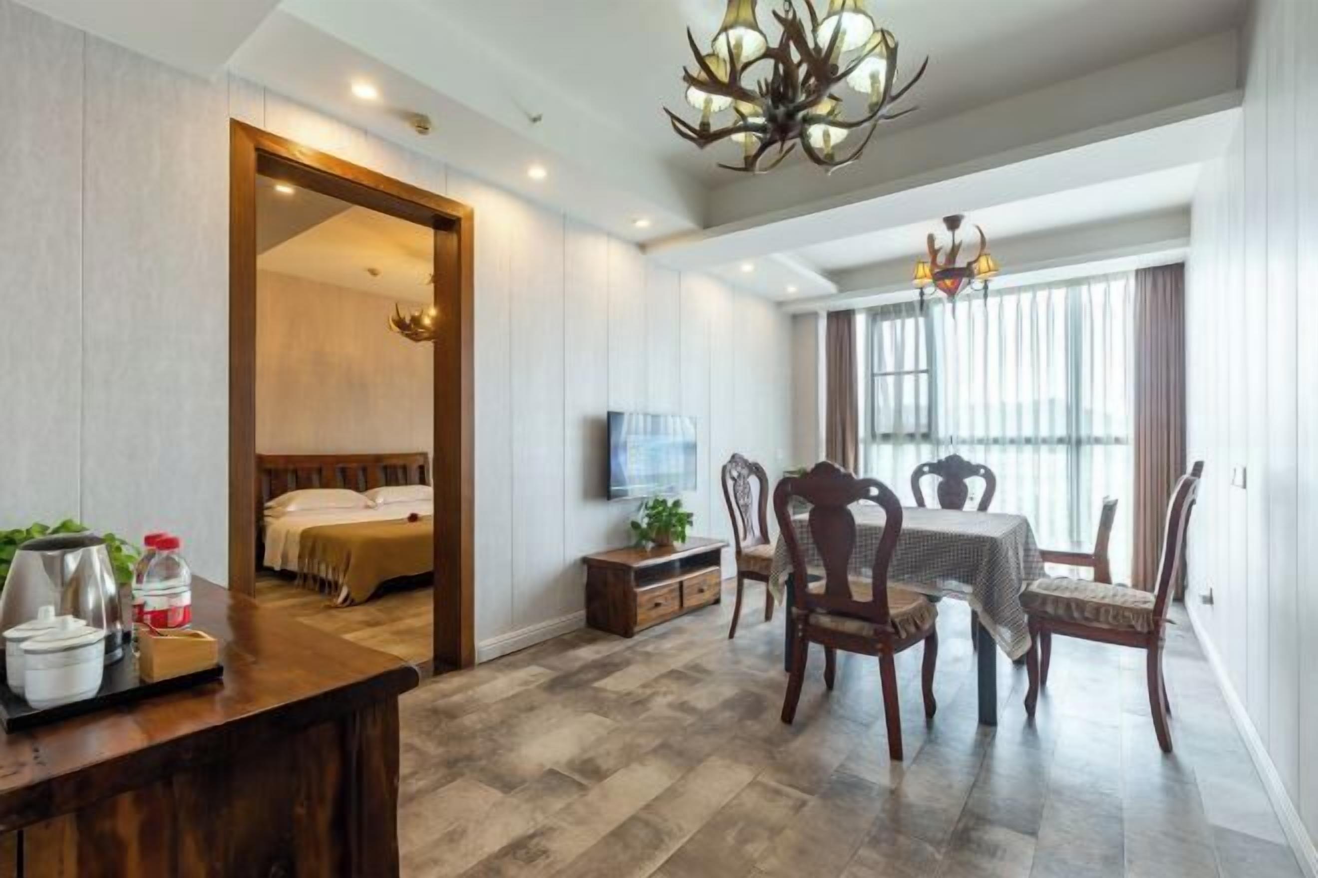 Habitación de hotel con piso de madera, un comedor con mesa y sillas, un televisor en la pared y una araña.