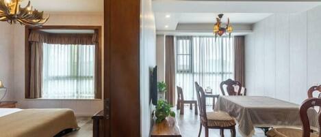 A hotel room with a bed, a dining table with chairs, a wooden bench, and a chandelier.