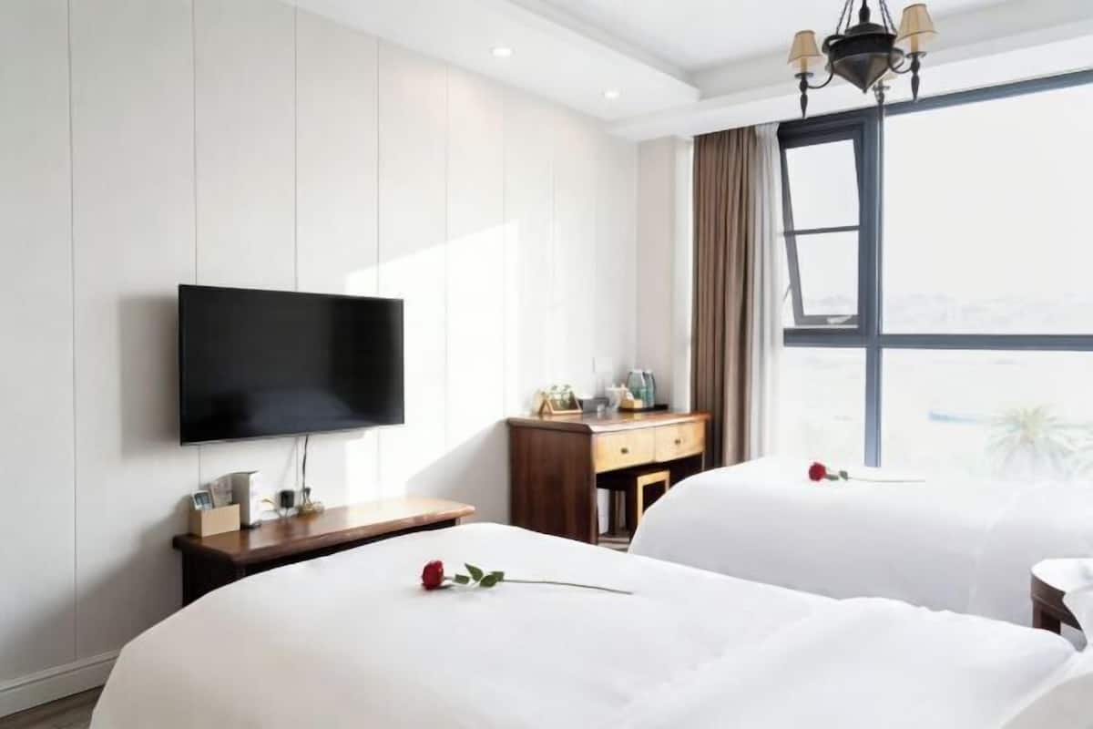 Quarto de hotel com duas camas, uma TV de tela plana, uma escrivaninha de madeira e uma janela grande com vista.