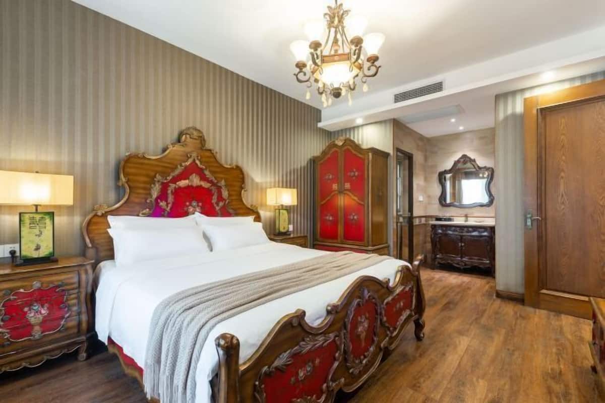 Quarto tradicional com uma cama grande, cabeceira ornamentada, um guarda-roupa de madeira e um espelho.