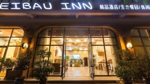 The exterior of the Eibau Inn with a clear entrance, potted plants, and a welcoming interior visible through the glass doors. - Aibao Hotel (Chongqing)