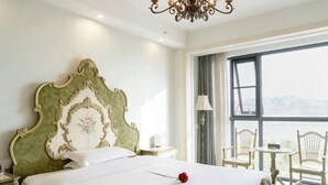 A hotel room with a large bed, a chandelier, a balcony with chairs, and a view. - Aibao Hotel (Chongqing)